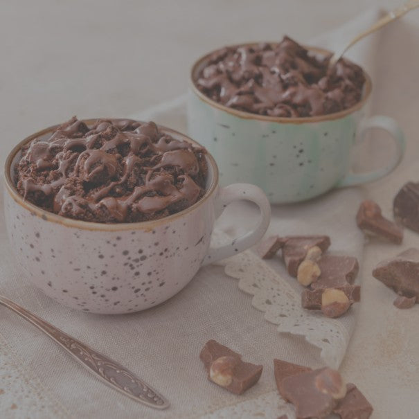 Two mugs of hot chocolate with whipped cream and chocolate pieces on a table.