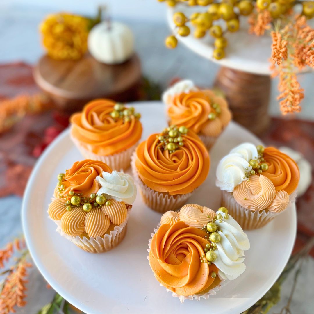 Six cupcakes topped with swirls of orange and white frosting, and gold sprinkles.