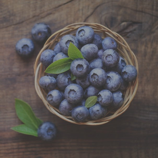 Basket of blueberries with a few scattered on a wooden surface