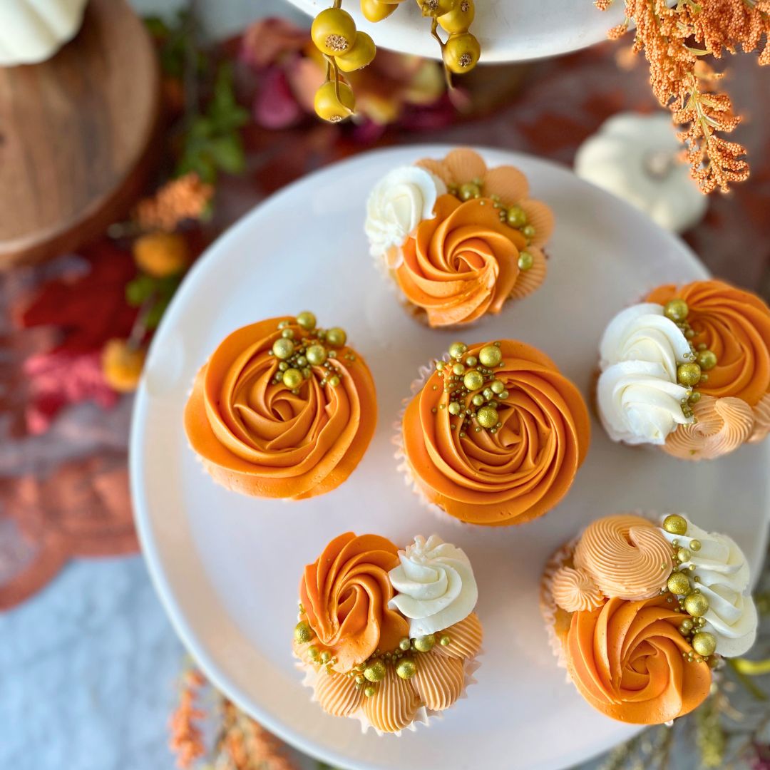 Six cupcakes topped with swirls of orange and white frosting, and gold sprinkles.
