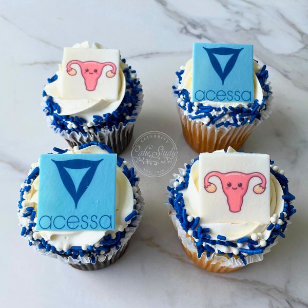 Four cupcakes, two topped with a blue square with a triangle and two with a white square with a pink uterus.