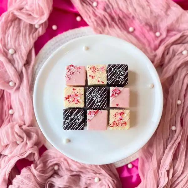 A set of three tiny, decorated tea cakes with a chocolate, raspberry, and vanilla flavor, presented on a plate with a pink and white floral .