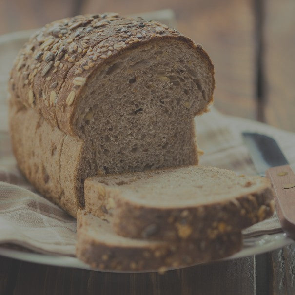 Loaf of whole grain bread with a few slices cut, on a wooden surface.