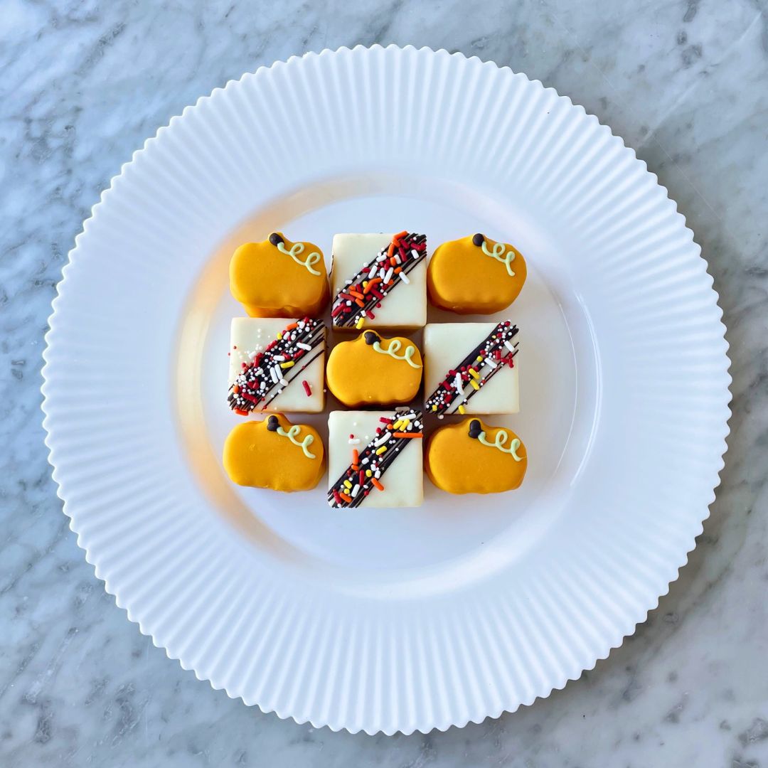 A small square cake with a chocolate drizzle and sprinkles, and a few miniature pumpkin-shaped cakes.