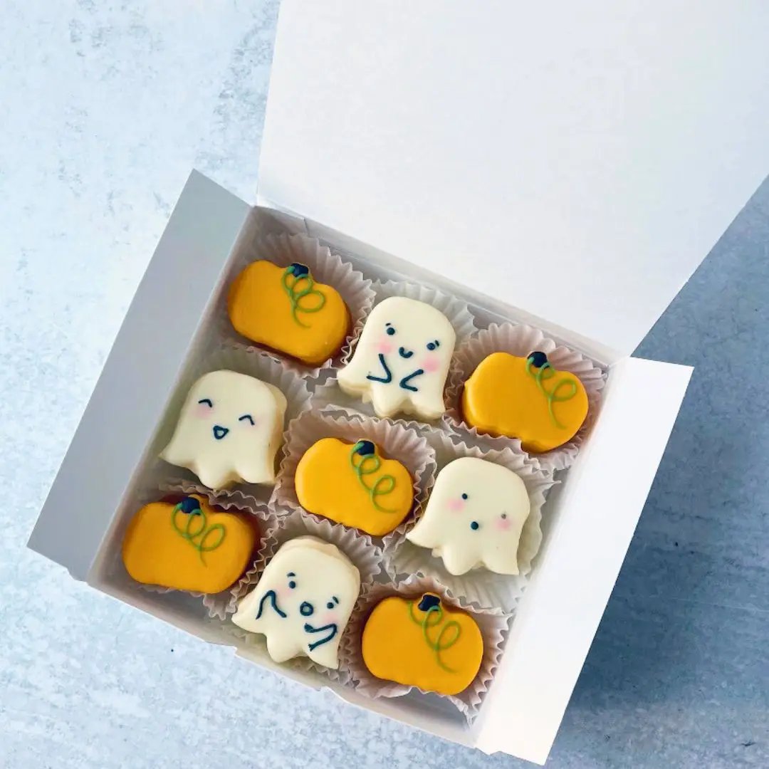 A top-down view of a box filled with white and orange cookies shaped like pumpkins and ghost.