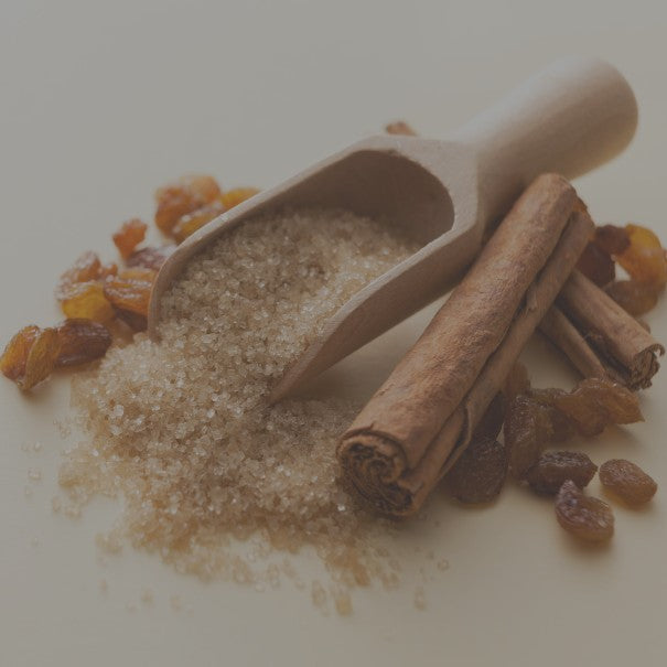 Wooden scoop with brown sugar, cinnamon sticks, and raisins