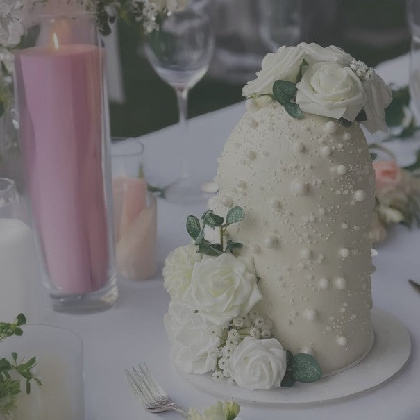 Decorative white cake with floral elements on a table setting with candles and glasses.