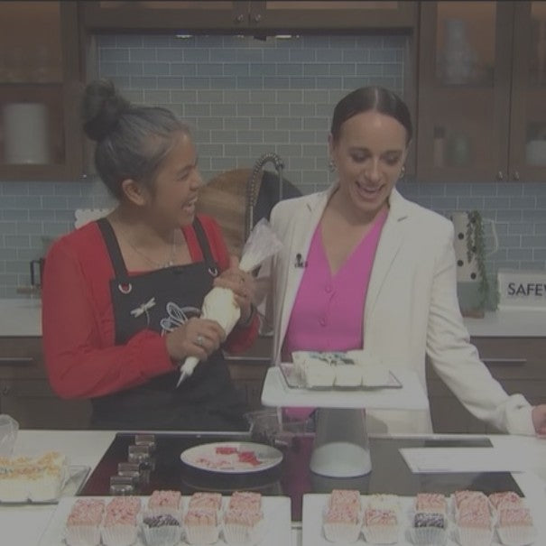 Two women in a kitchen decorating cupcakes with frosting.