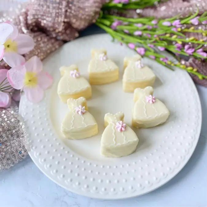 A plate of white chocolate candies shaped like dresses with pink bows