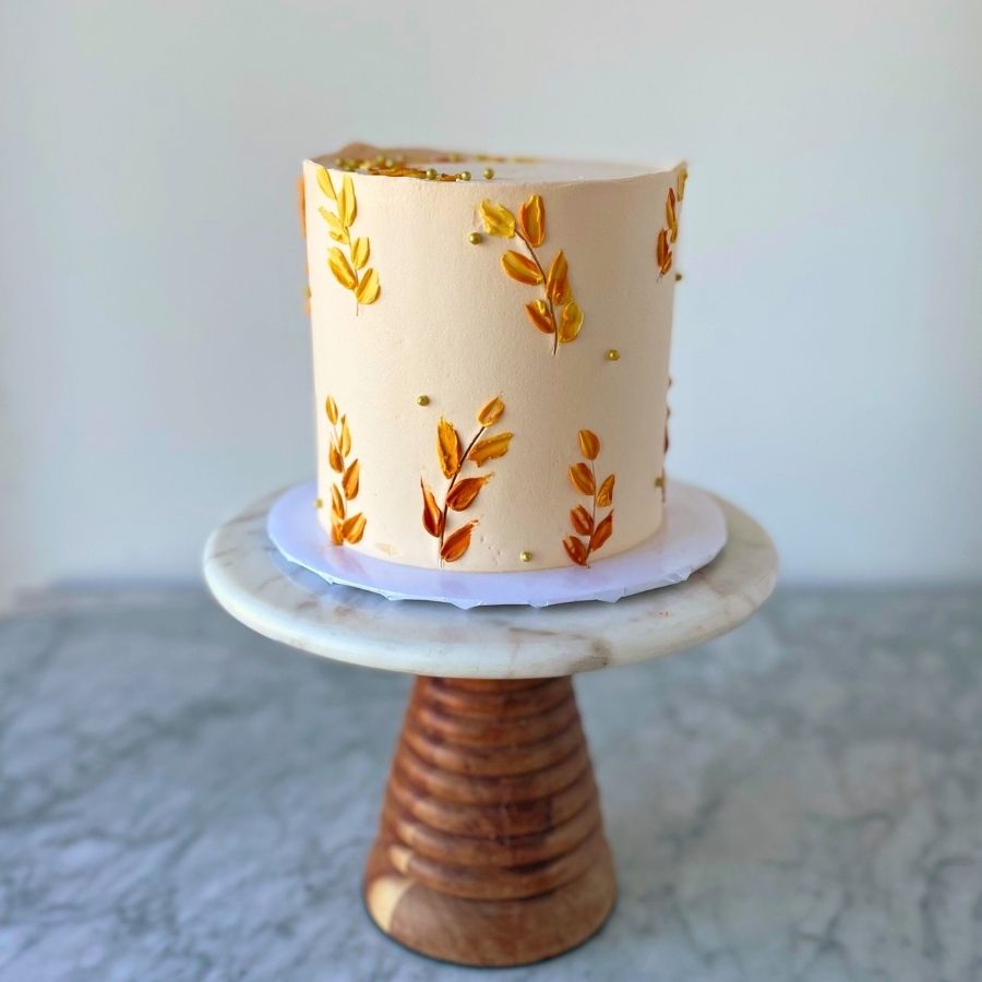 Decorative cake with leaf patterns on a marble stand against a neutral background