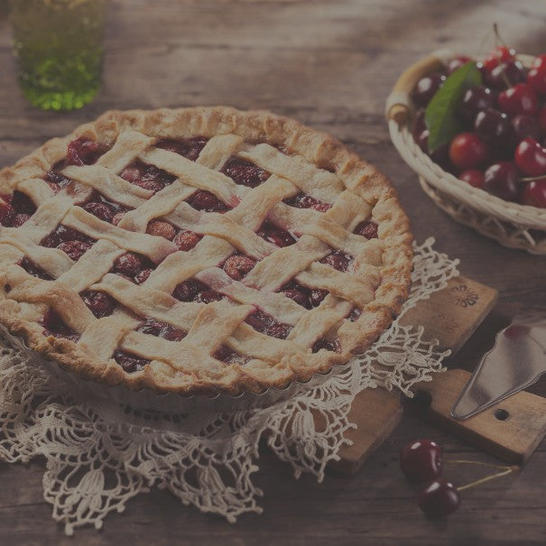 Cherry pie with lattice crust on a wooden table with a basket of cherries.
