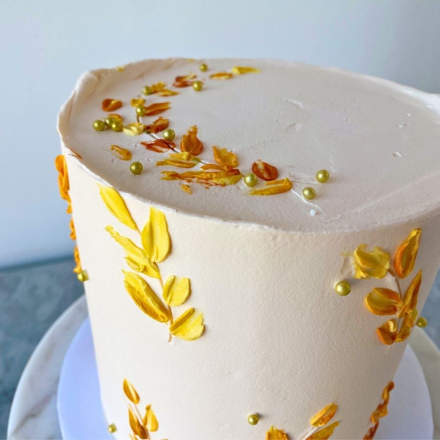 Close-up of a cake with white frosting and yellow leaf decorations on a light background