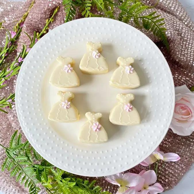A plate of white chocolate dress-shaped candies surrounded by pink flowers