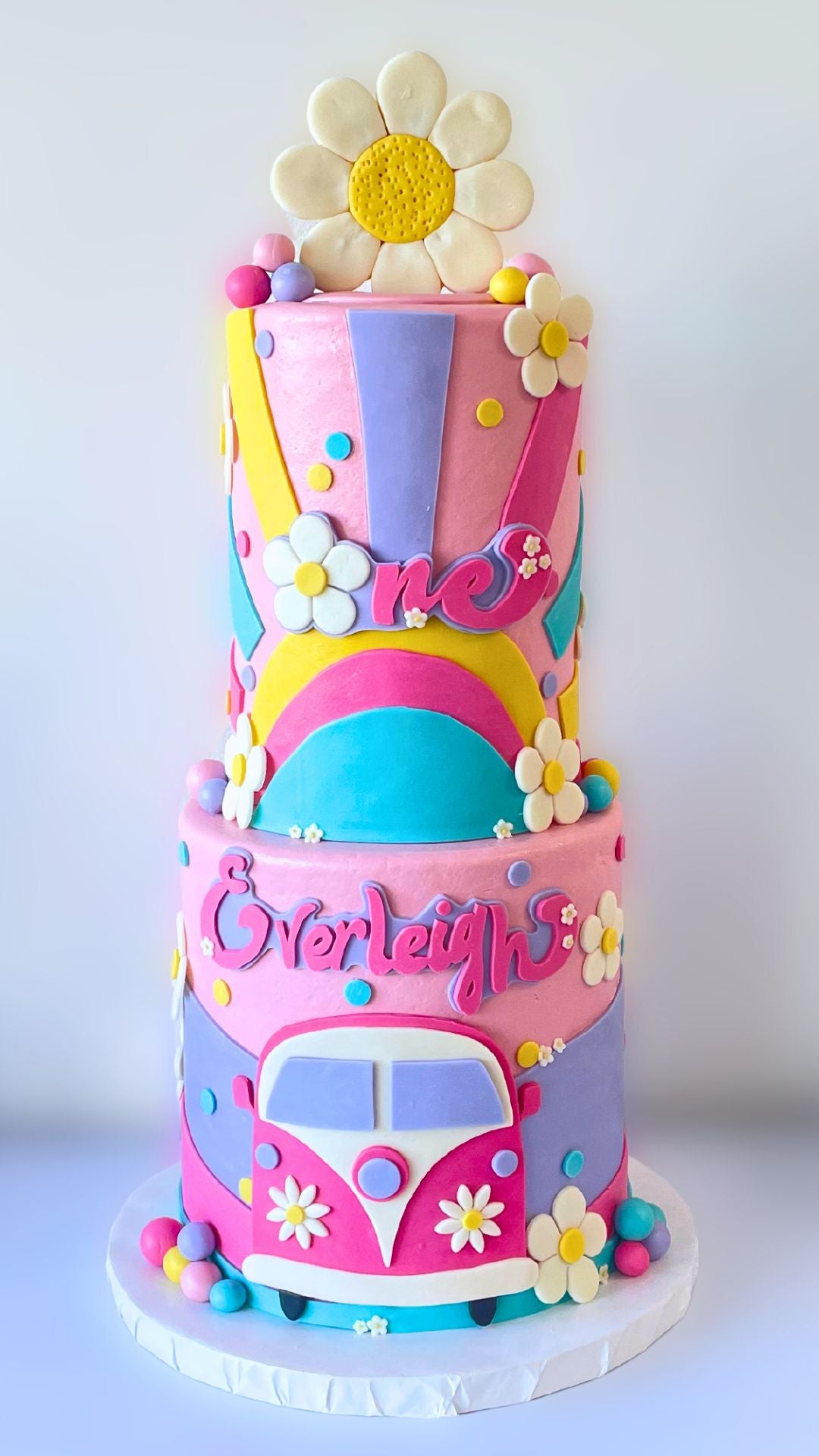 A tall two-tiered cake decorated with various colorful, layers of pink, purple, blue, and a flower frosting.