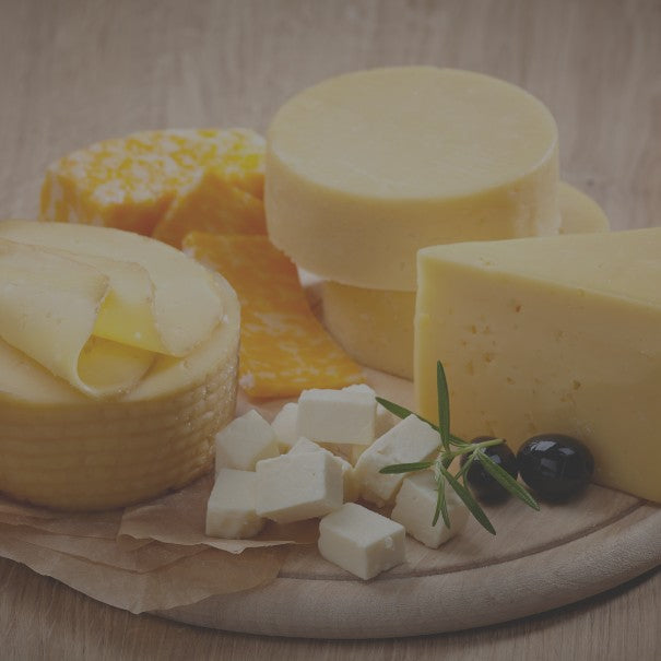 Assorted types of cheese on a wooden board with a neutral background