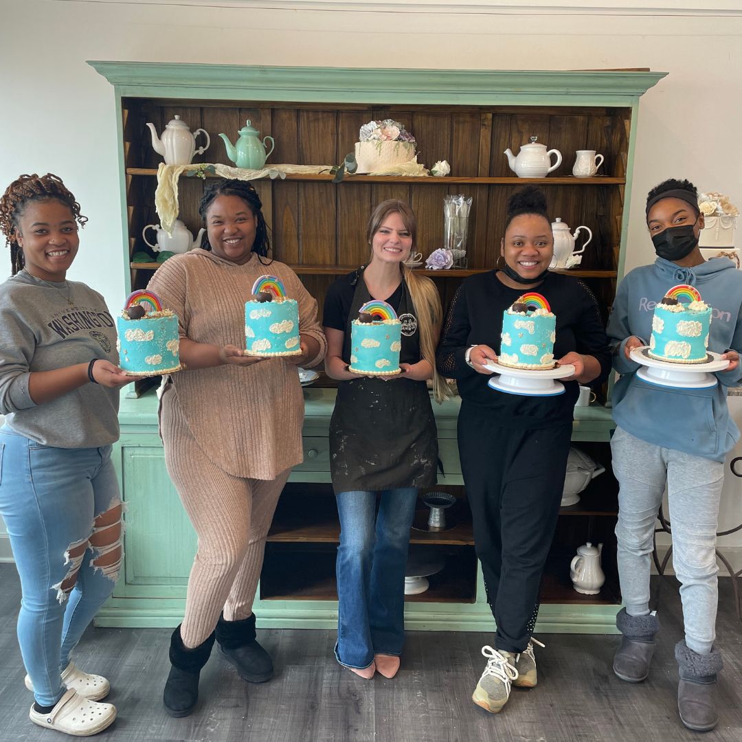 five women holding a blue cake