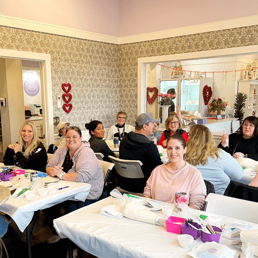 A group of people that are participating in a baking and decorating class, with some various baking supplies on the table in front of them.