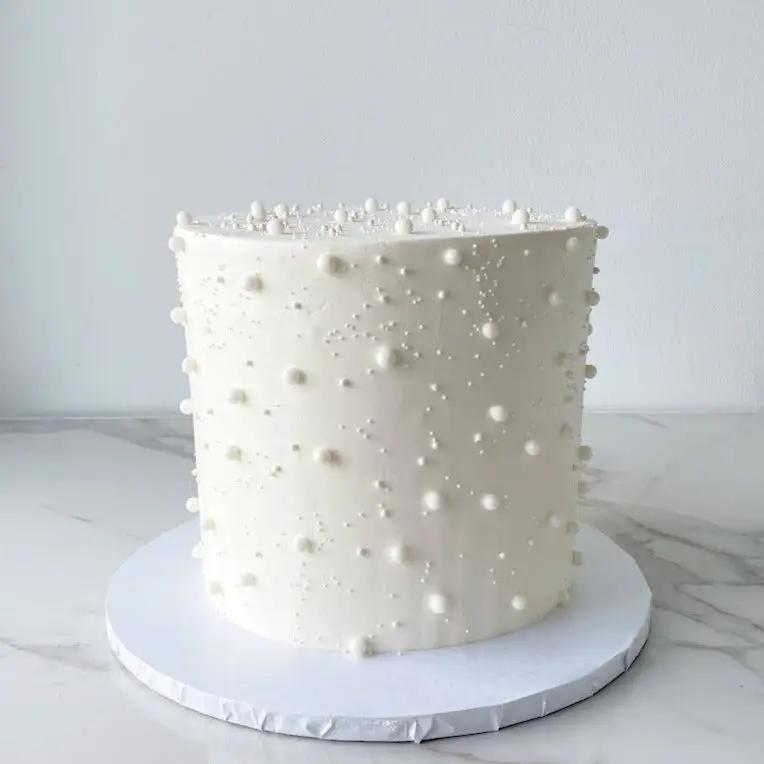A small white cake with small pearl-like beads covering the sides.