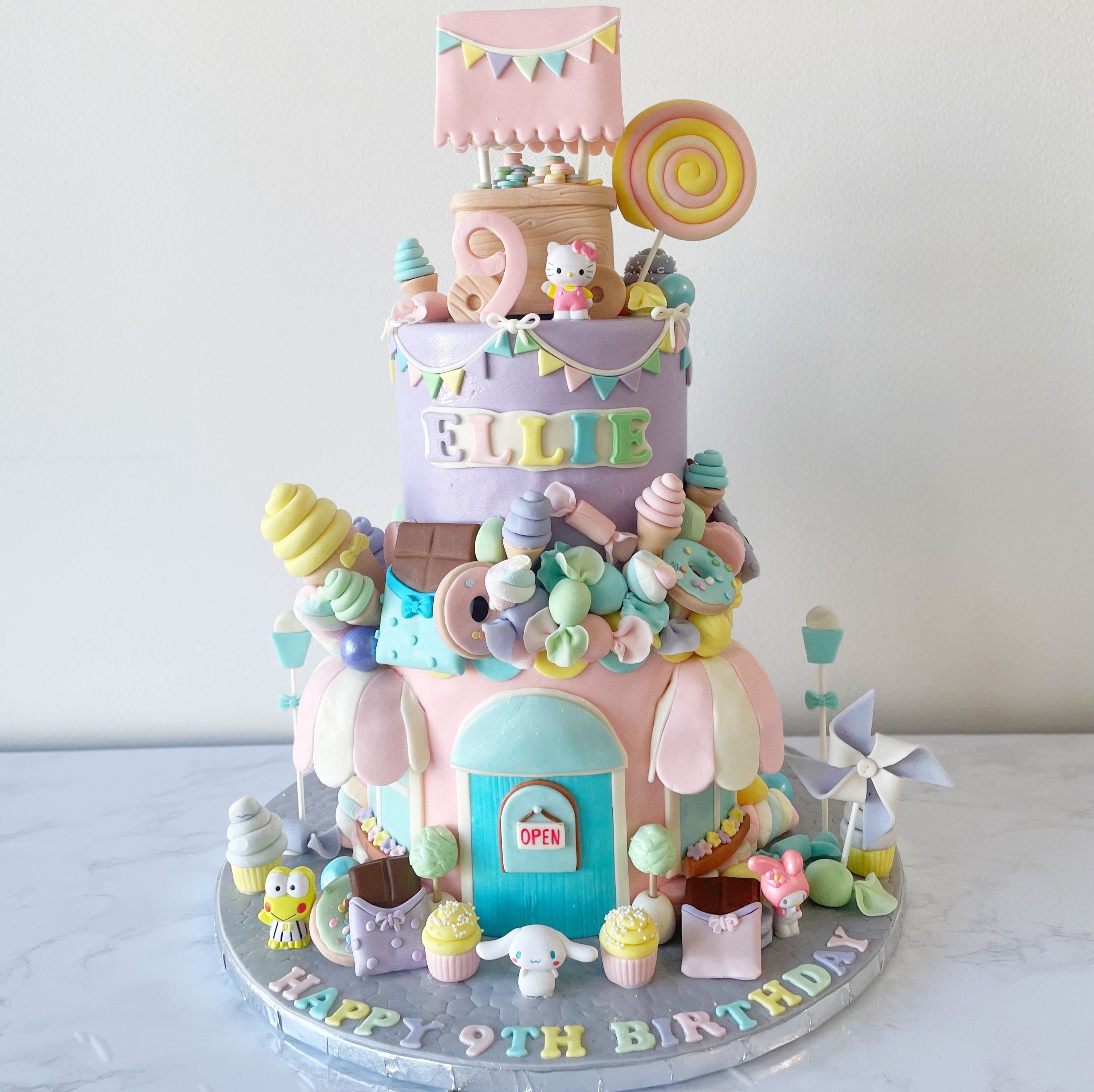 Multi-tier pastel cake with colorful decorations including rainbows, stars, and cartoon elements, perfect for a kids' party