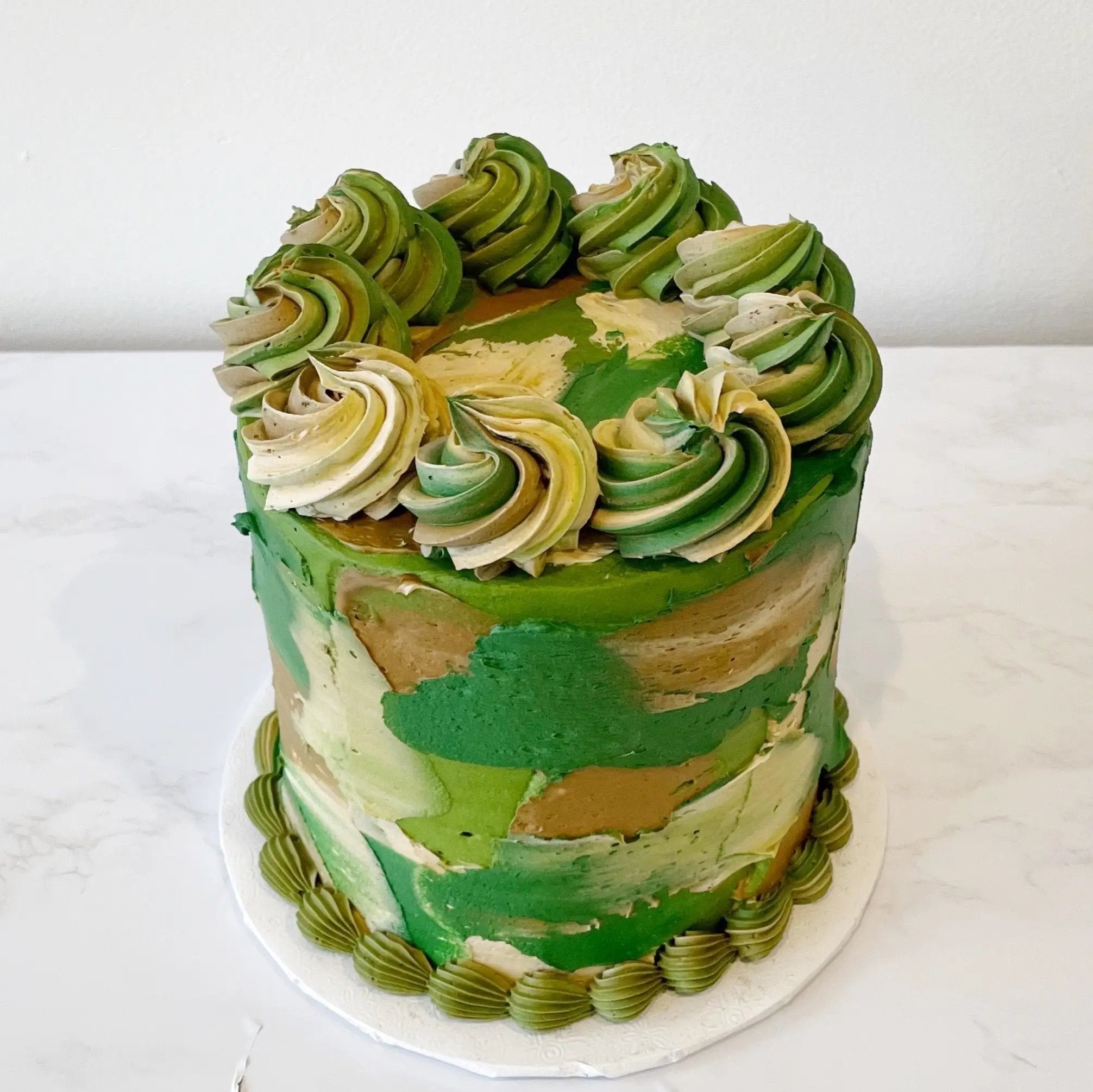 A single-tiered cake with green, brown, and white patterned icing and a green swirled top.