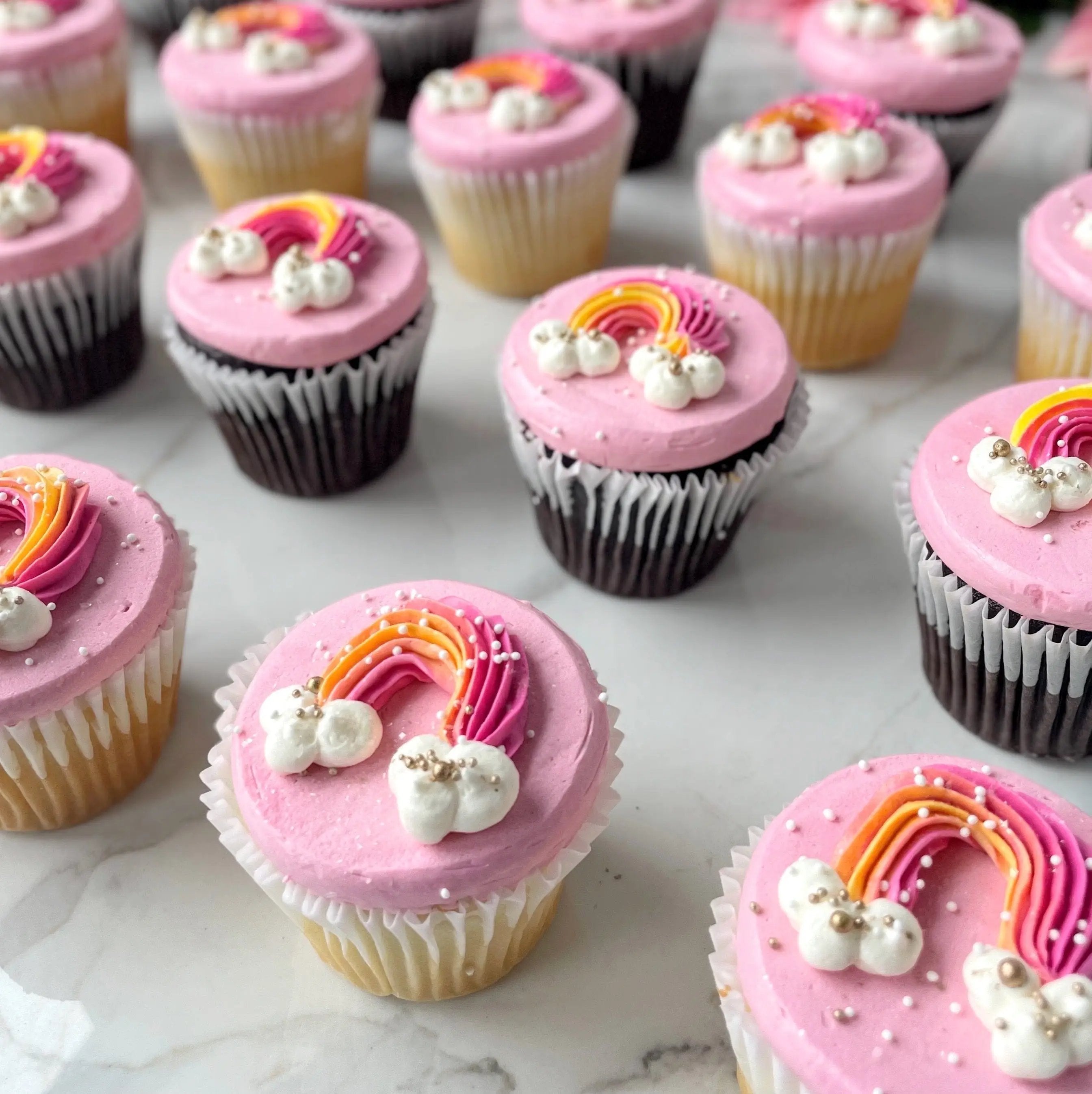 A top-down view of cupcakes with pink frosting, decorated to look like rainbows.