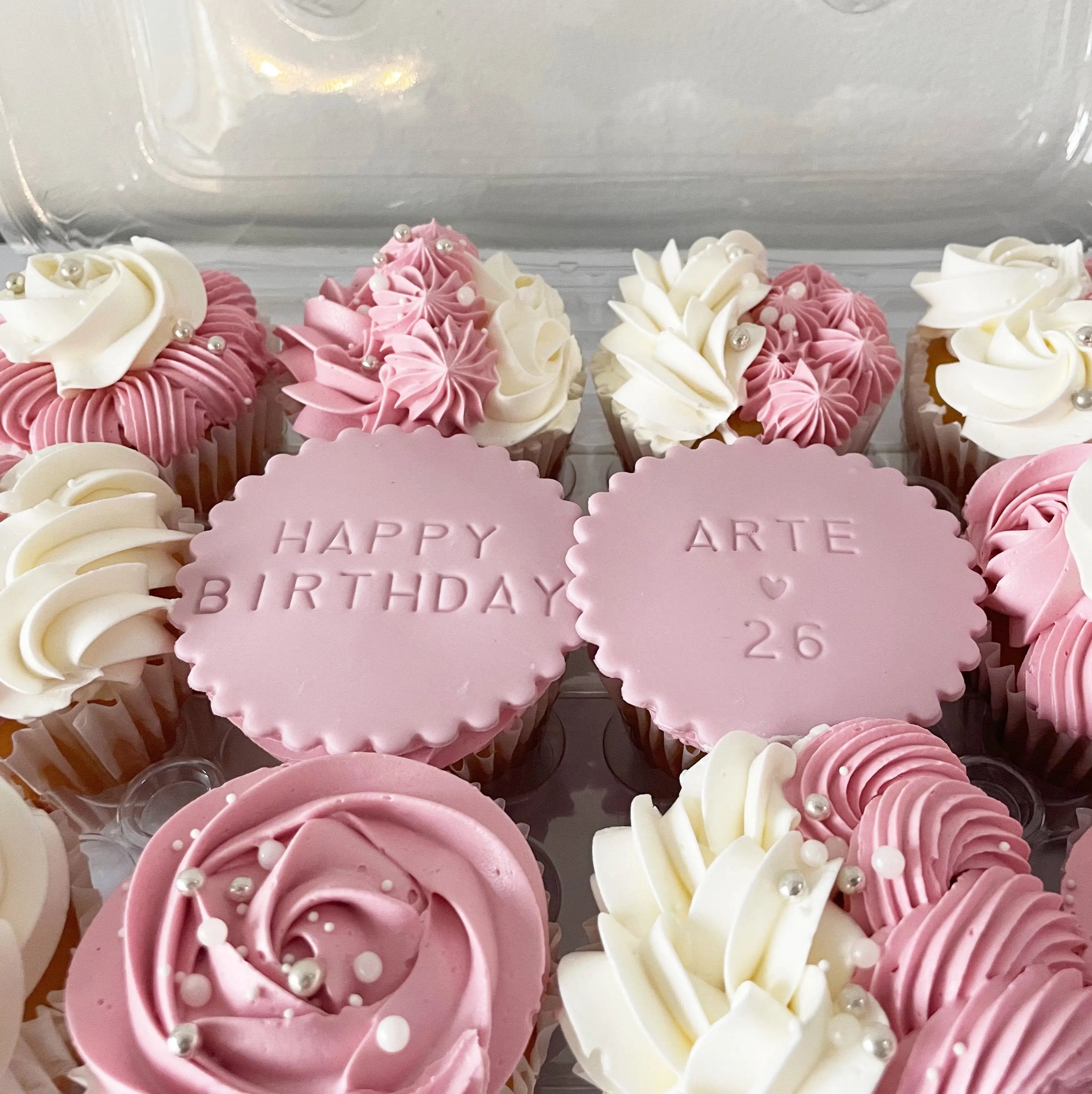 A close-up, top-down view of the tray of cupcakes with pink and white frosting.