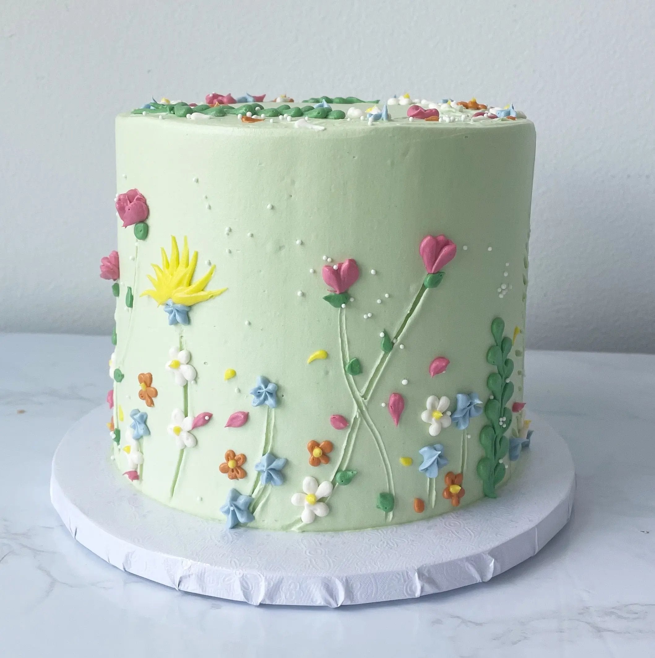 Green buttercream cake decorated with spring flowers and piping details