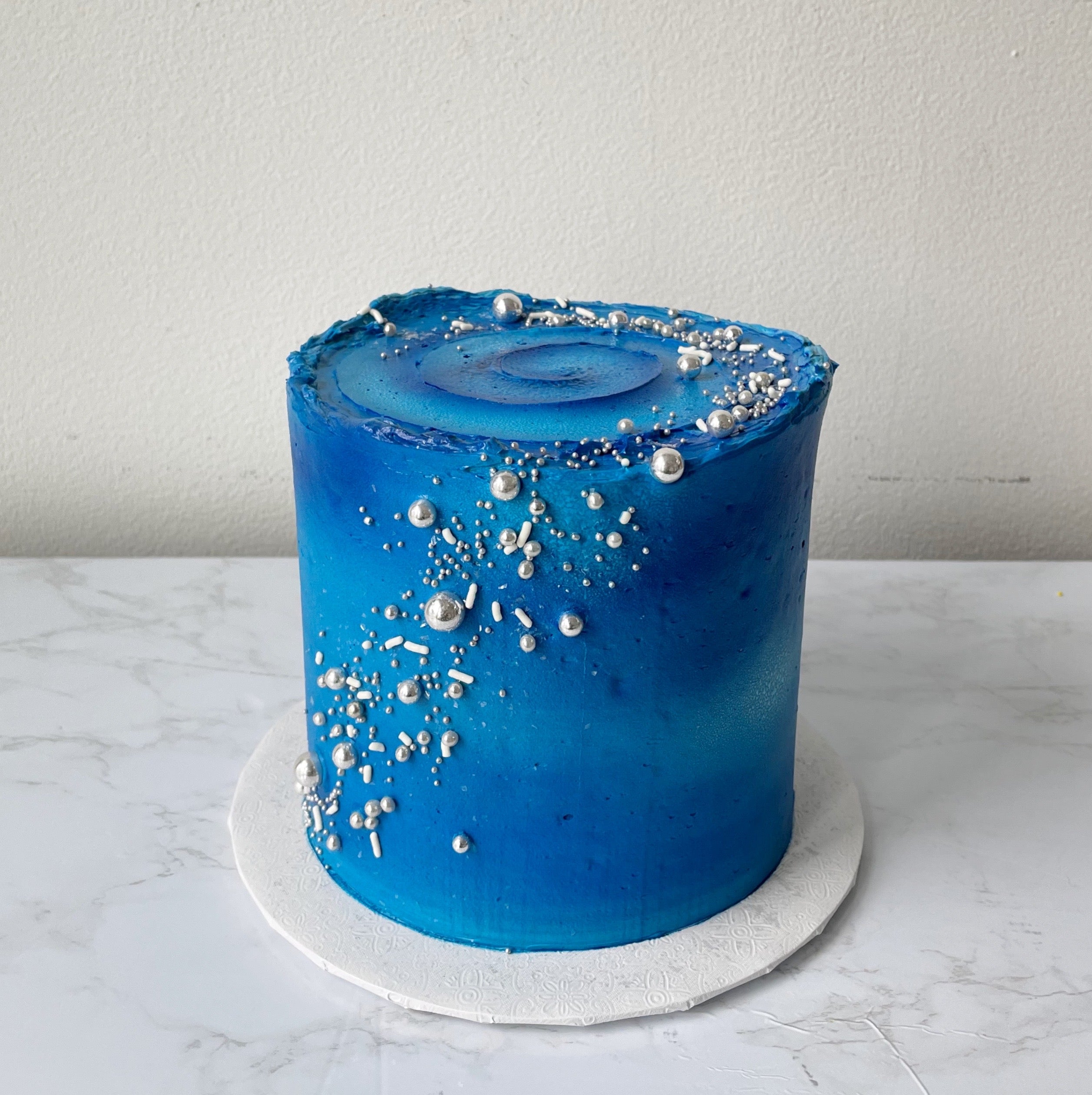 Blue frosted cake with gold stars and white specks on a marble background