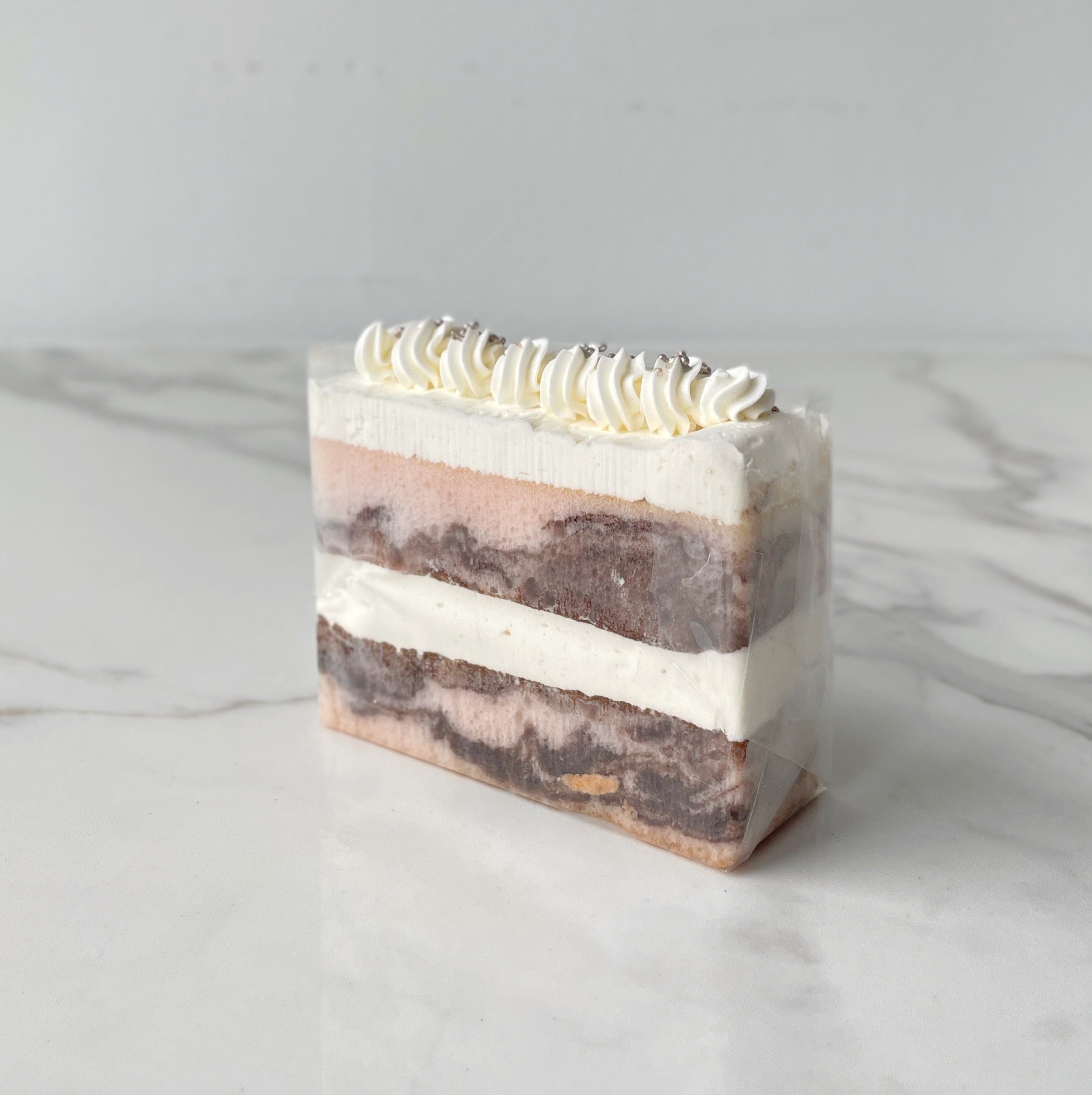 Chocolate and vanilla layer cake slice topped with whipped cream and chocolate drizzle