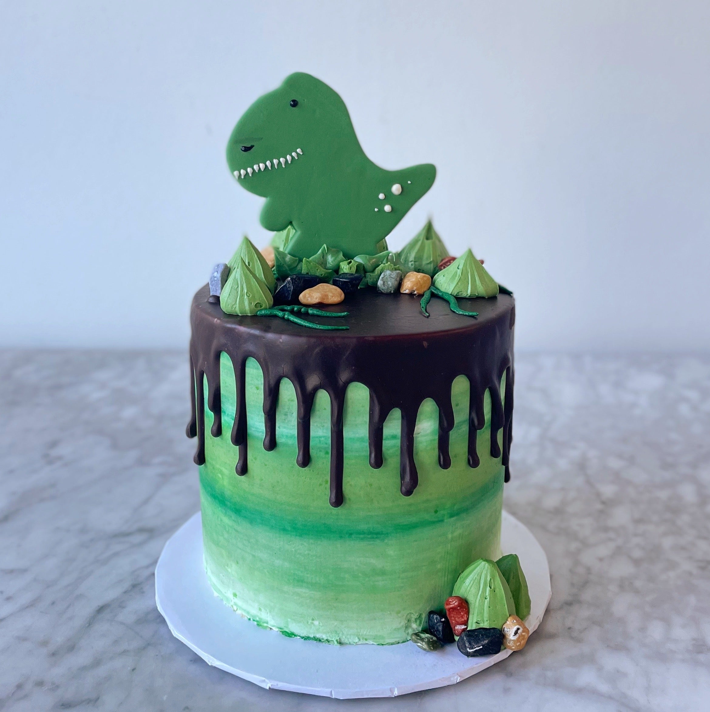 Green dinosaur-themed cake with chocolate drip icing