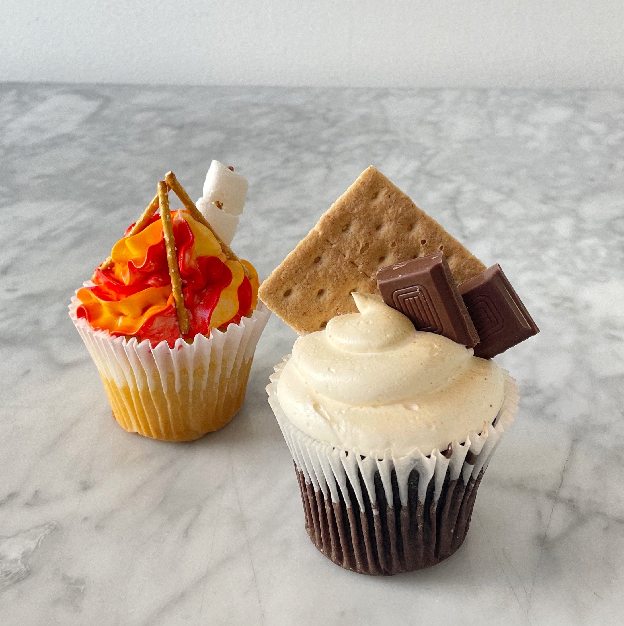 Two Thanksgiving cupcakes, one decorated with biskets and chocolate and other with orange frosting