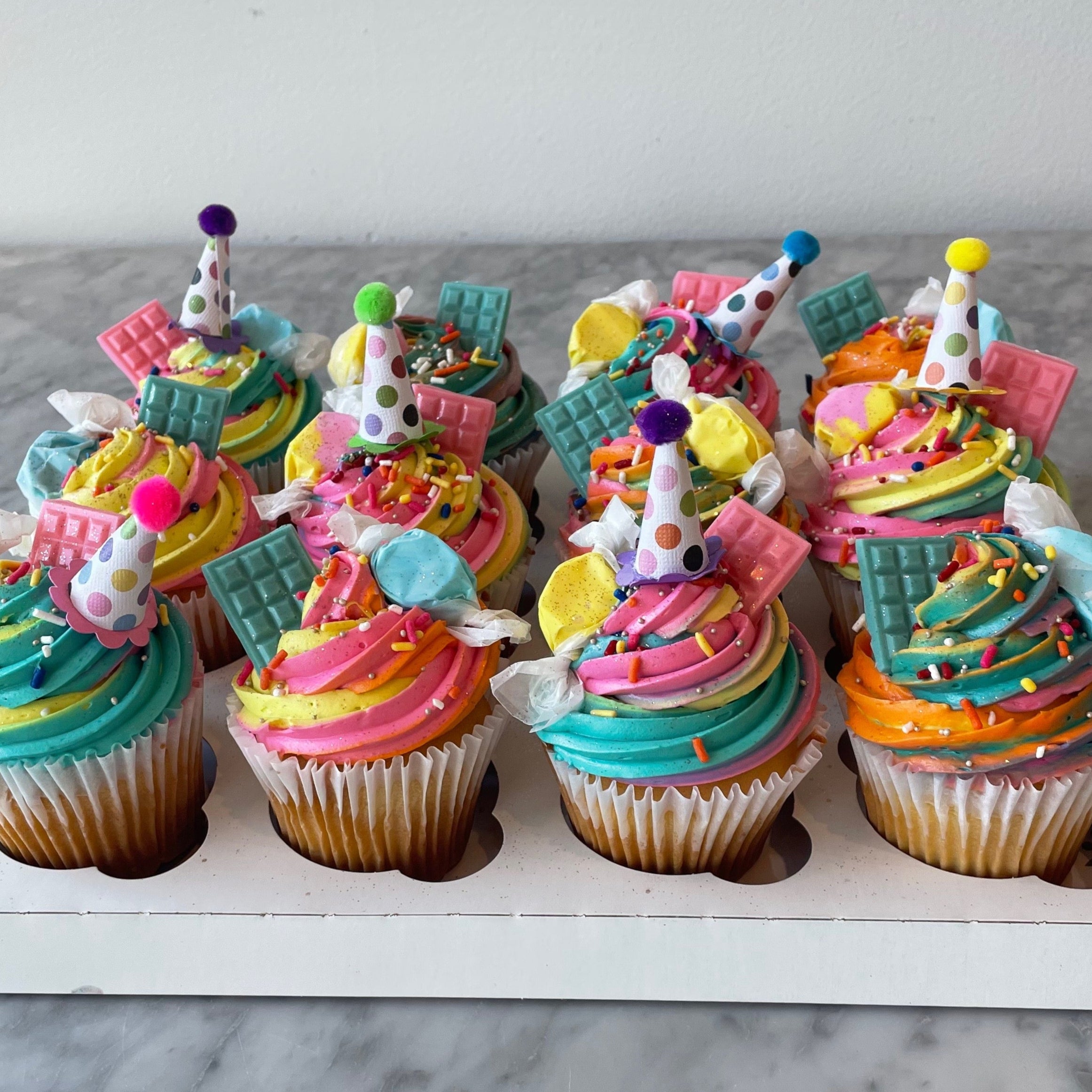 Brightly colored rainbow cupcakes topped with swirled frosting and fondant