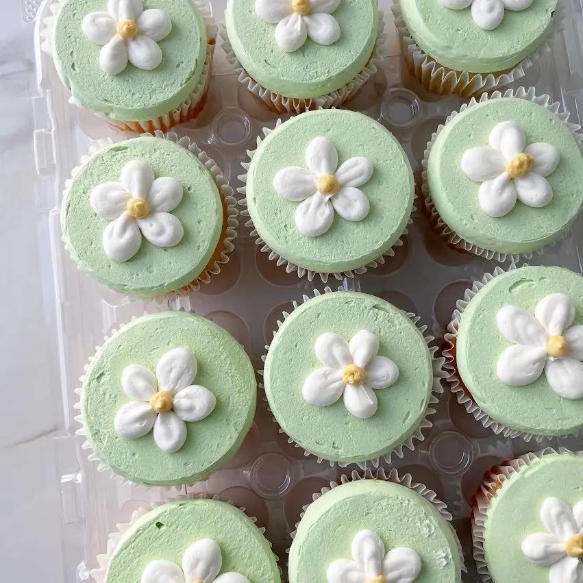 A tray of frosted cupcakes with light green frosting. Each cupcake is decorated with a small white and yellow daisy in the center.