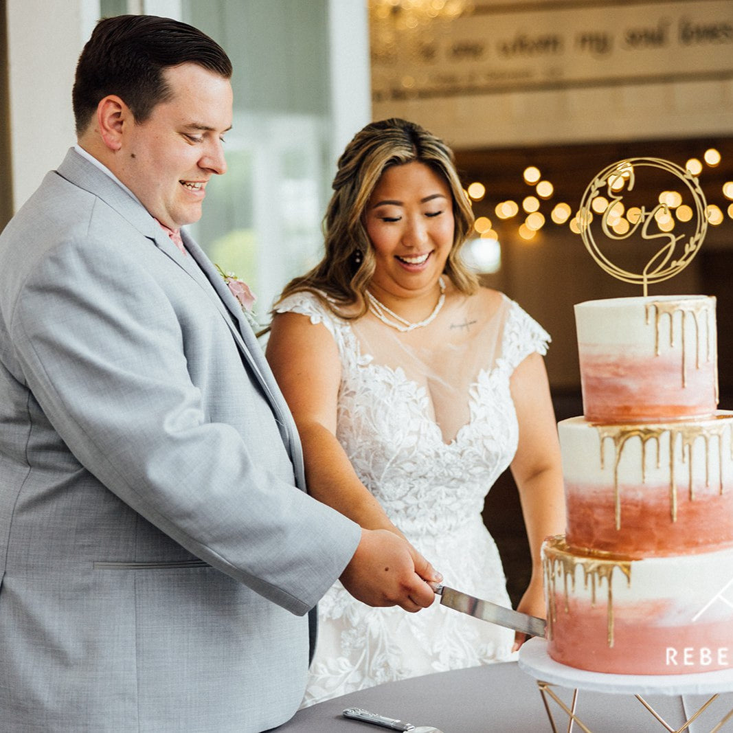 Smiling bride and groom cutting a pink ombré wedding cake together during their wedding reception in a warmly lit venue