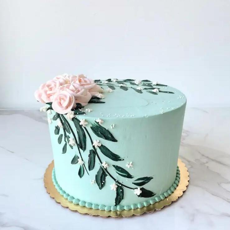 A light blue cake decorated with a pink flower and green leaves on the side.