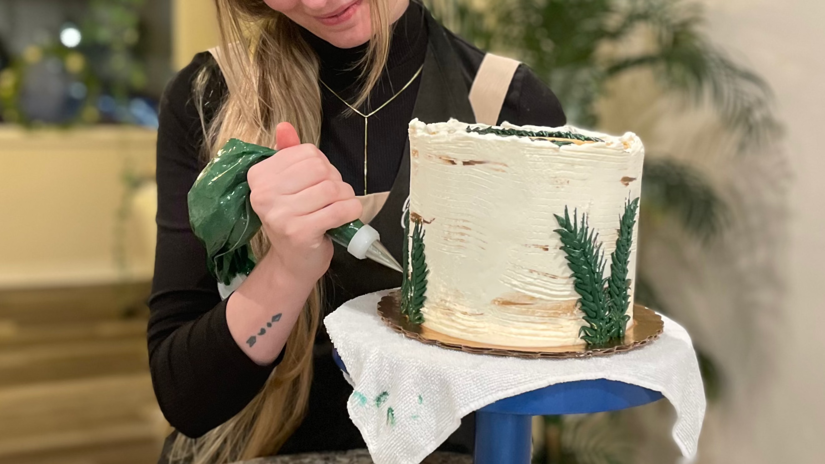 Baker decorating a cake with frosting while holding a piping bag, focusing on details during a cake decorating process