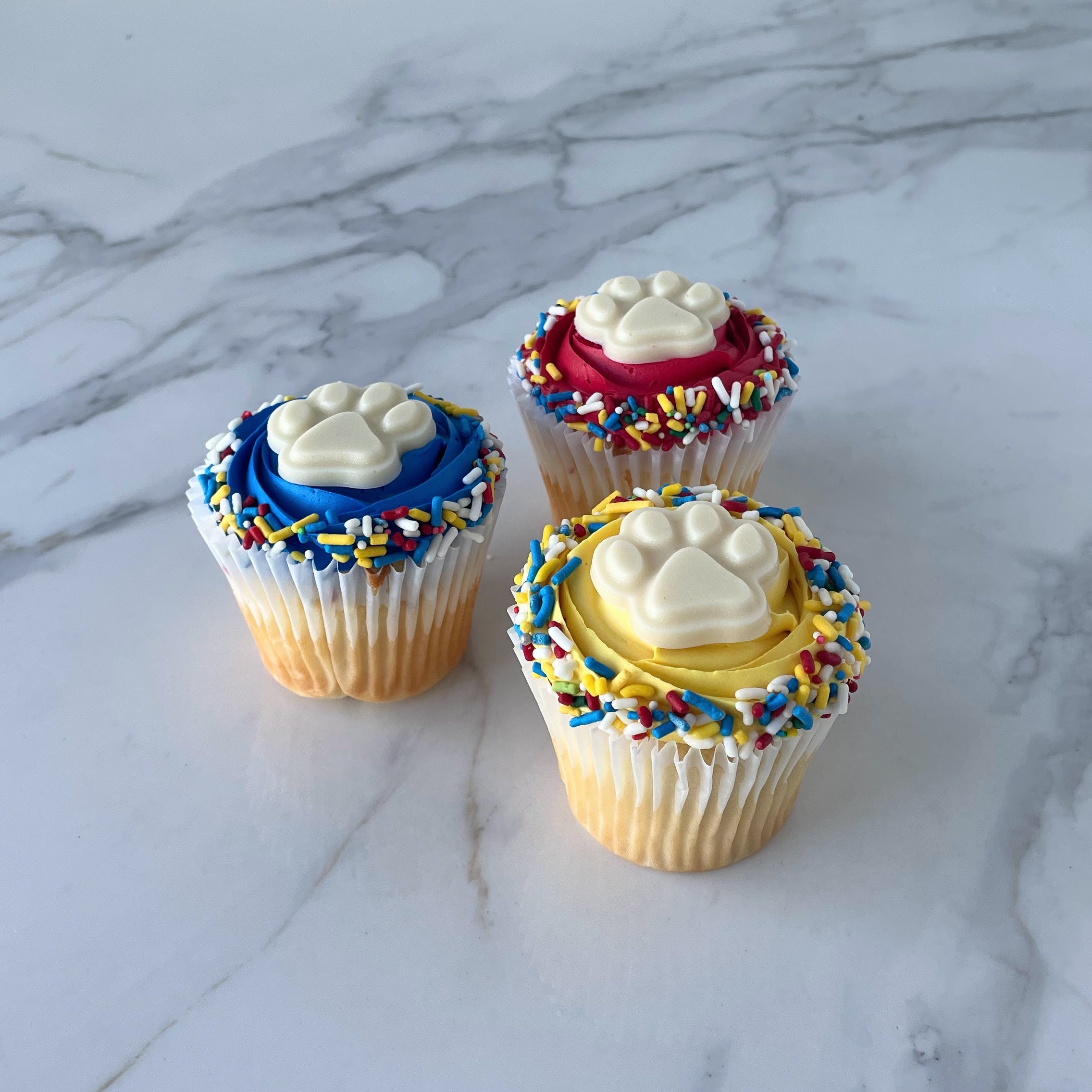 Three cupcakes with colorful frosting and toppings on a marble surface