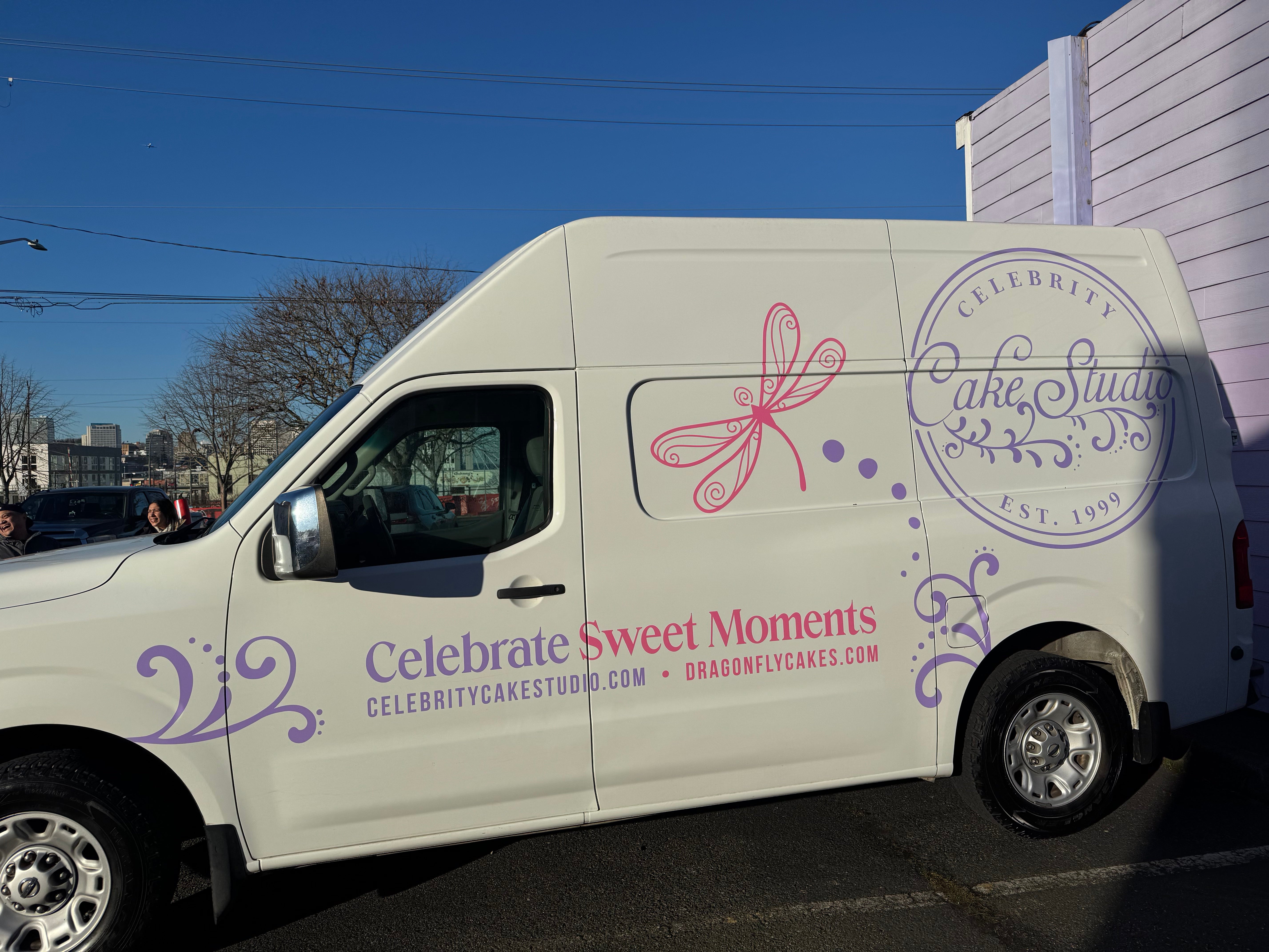 White delivery van with 'One Dozen & Co.' branding and a cupcake logo, parked in a lot under a clear blue sky