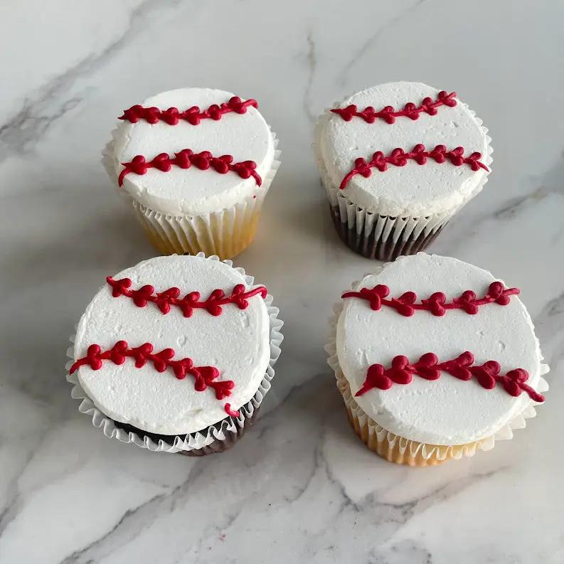 Four cupcakes with white frosting. Each cupcake is decorated with two red lines to look like a baseball.