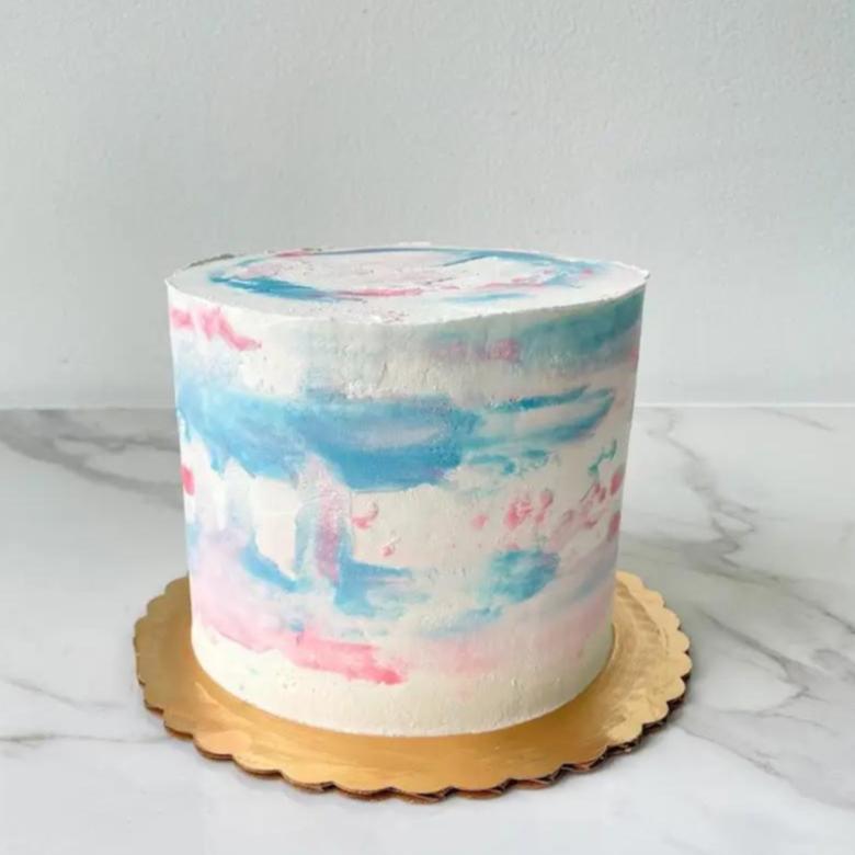 A tall, round cake with a white frosting that has a watercolor effect of light blue and pink.