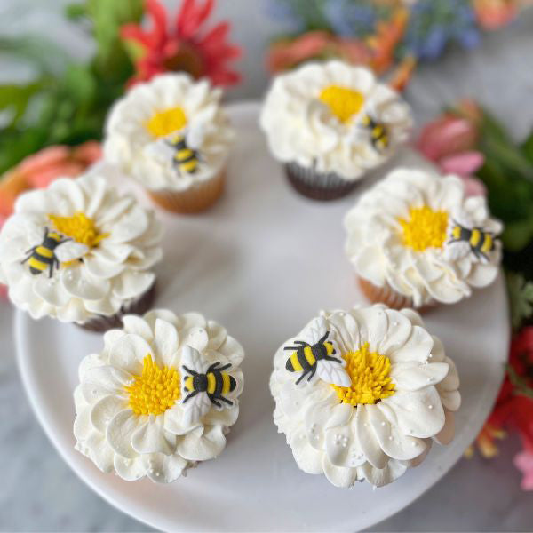 Cupcakes topped with white buttercream flowers and fondant bees, arranged in a circle