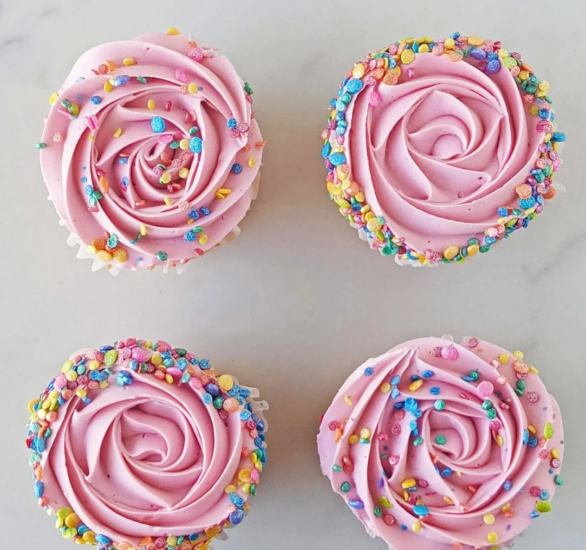 A square of four cupcakes with pink frosting and colorful sprinkles