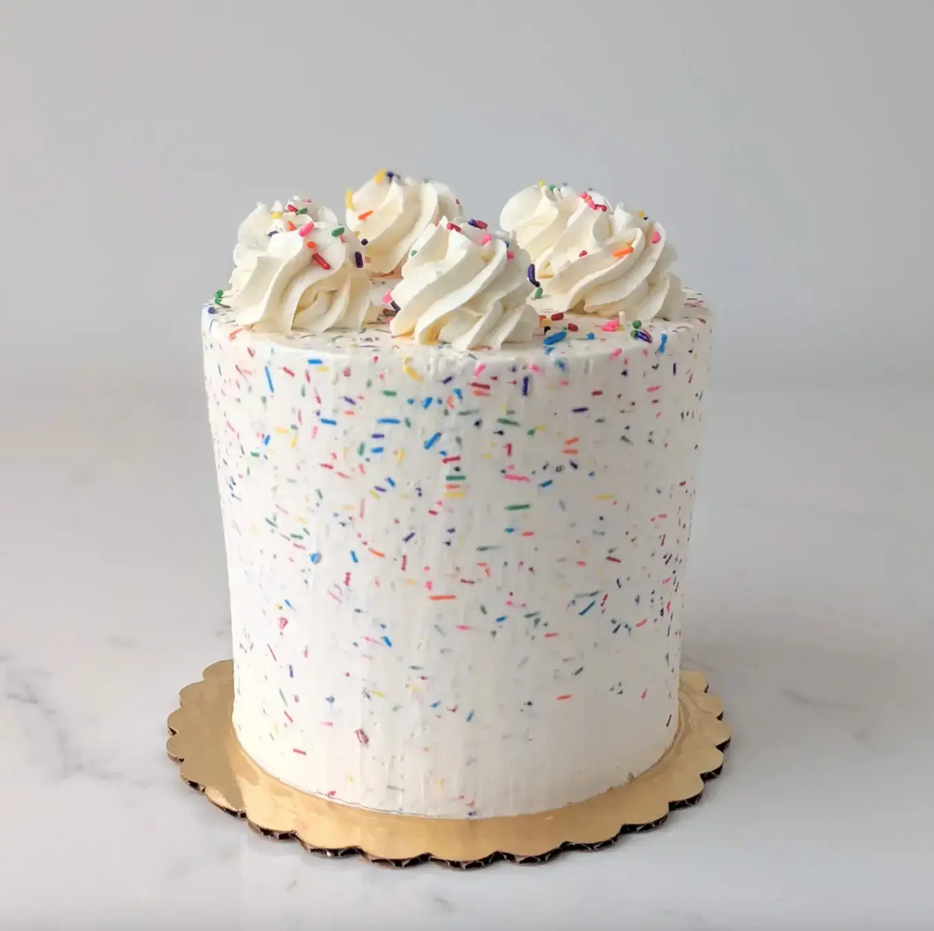 Celebration cake with white frosting, vibrant sprinkles, and piped floral decorations