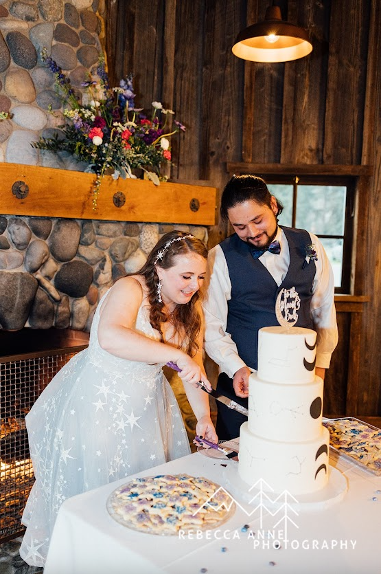 Elegant bride and groom standing together while preparing to cut their wedding cake in a warmly decorated reception hall
