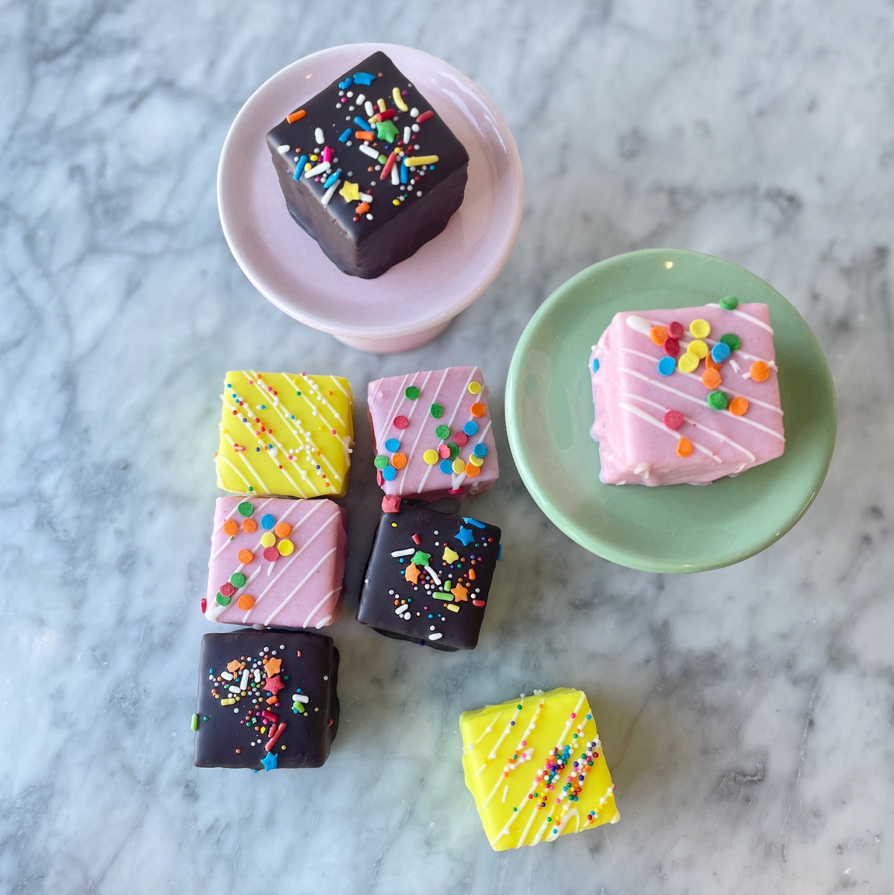 Colorful square petit fours with sprinkles on a marble surface