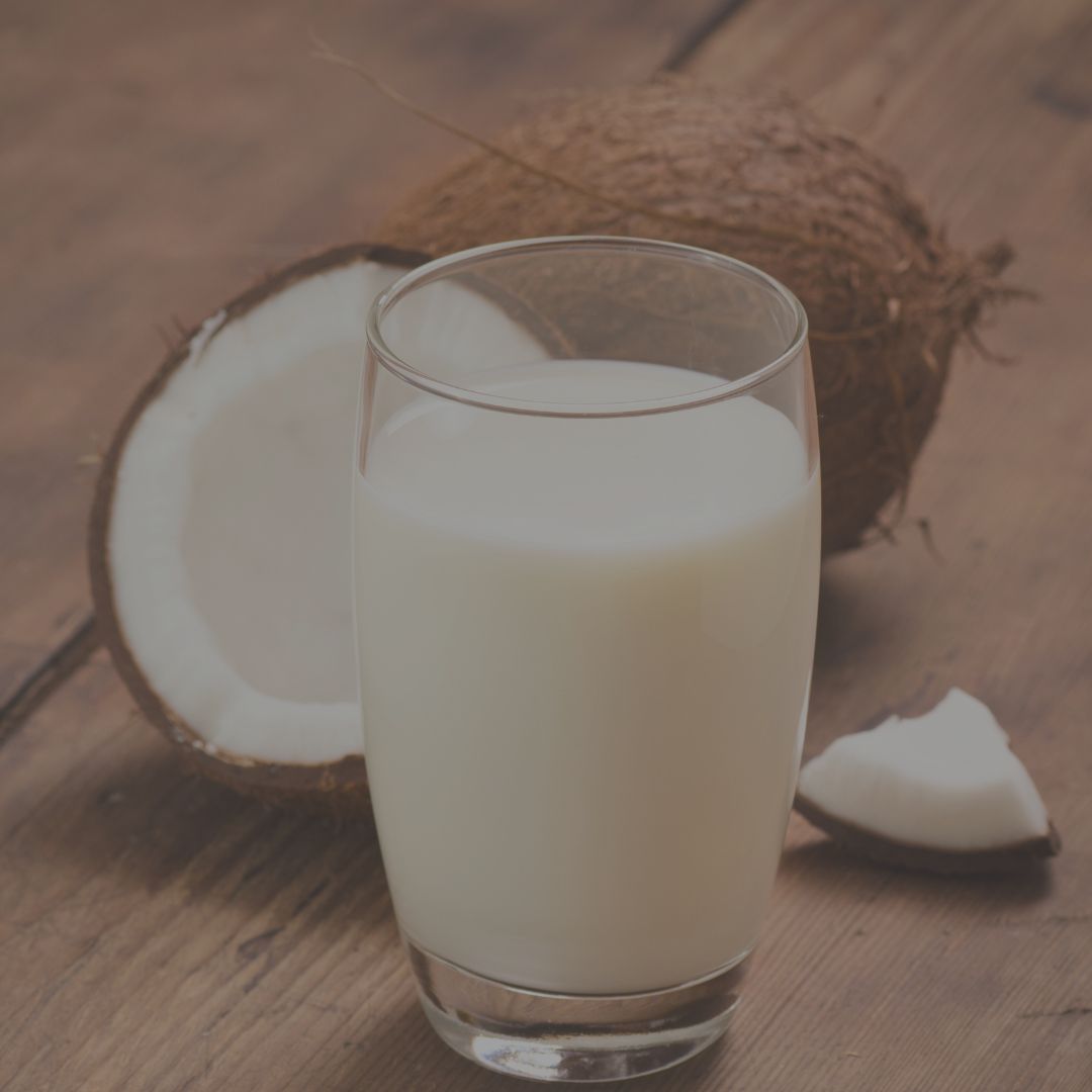 Glass of coconut milk with a whole coconut and a half coconut on a wooden surface
