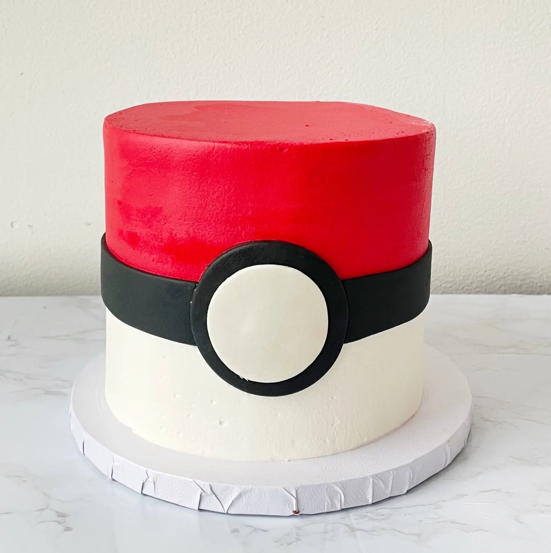 A round cake with a red top layer and a white bottom layer, decorated with a black circle and a white target-like design on the side.