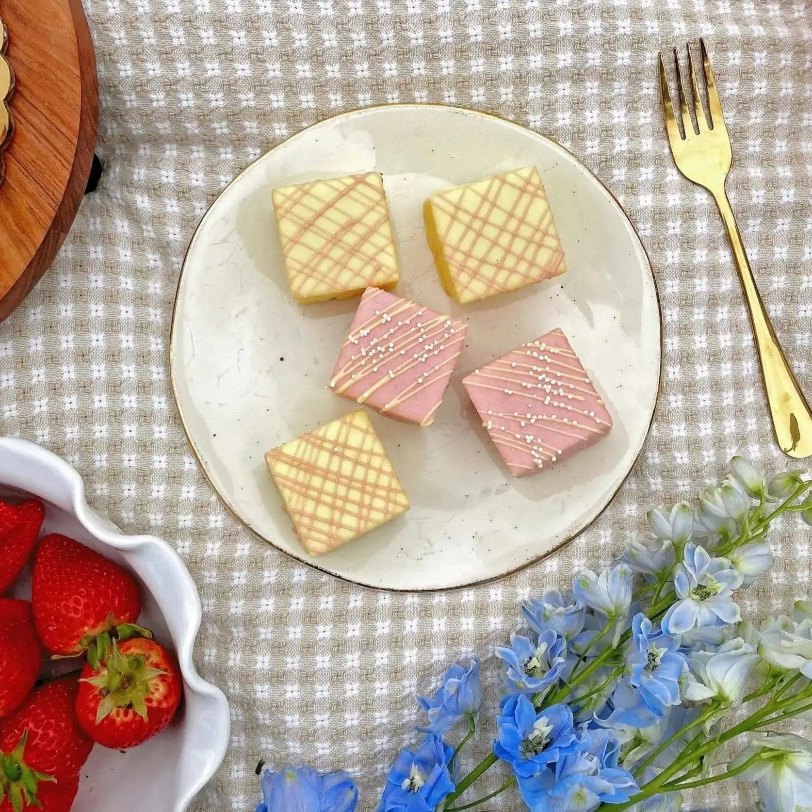 Plate of square cookies with pink and yellow checkered patterns.