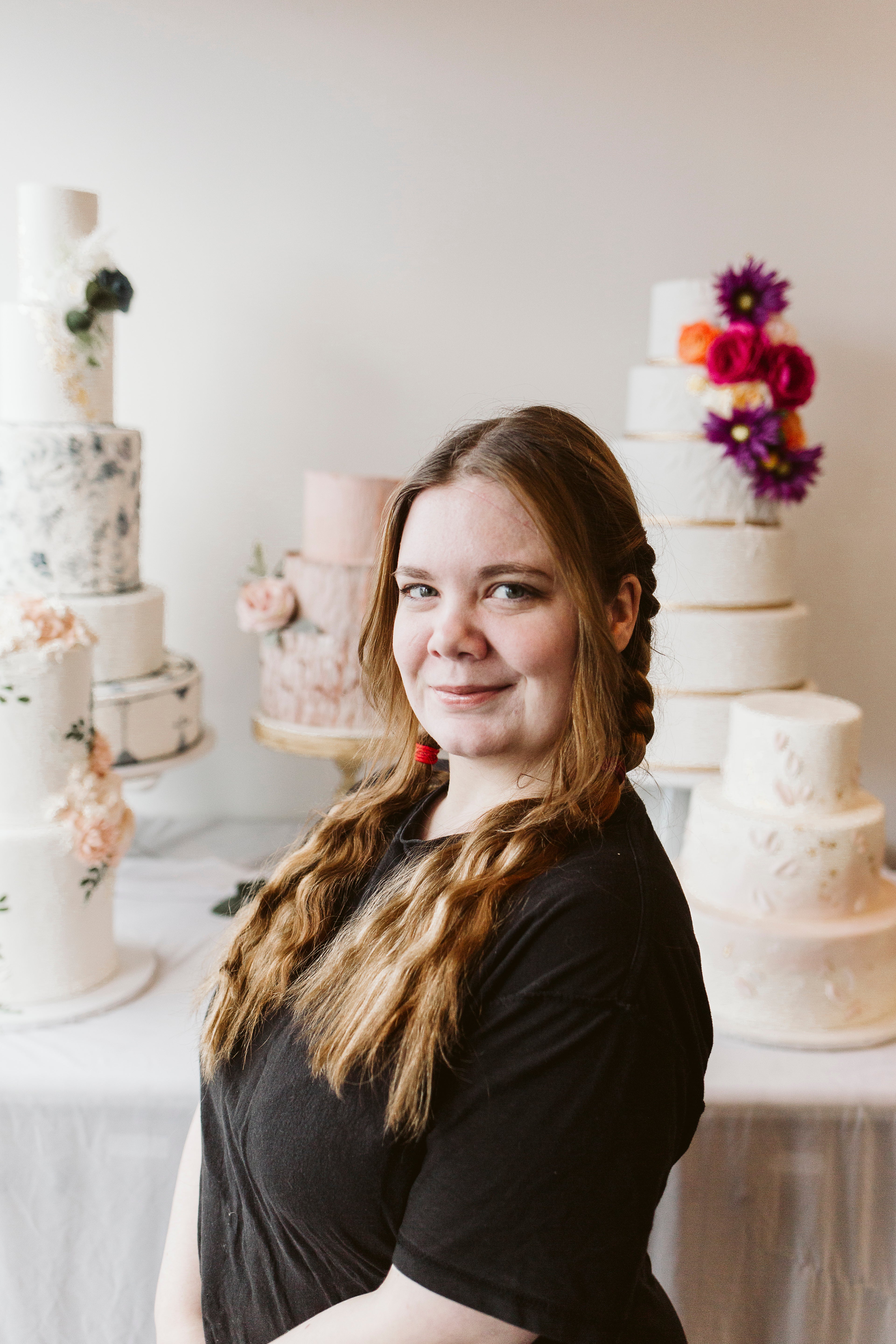 Woman with long blonde hair smiling and posing in front of a floral-themed cake display