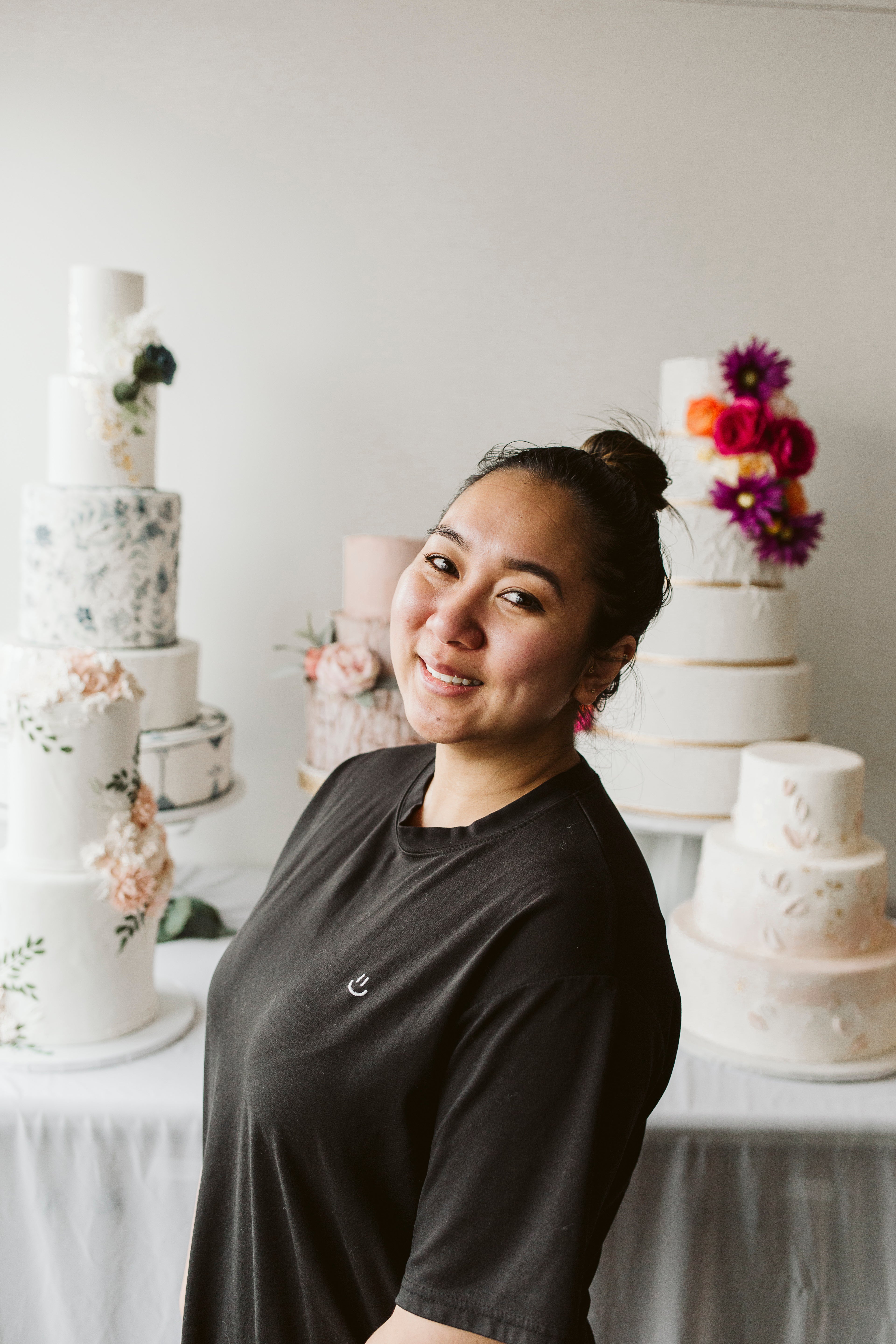 Portrait of a smiling woman with a red flower in her hair, standing in front of a decorated cake.